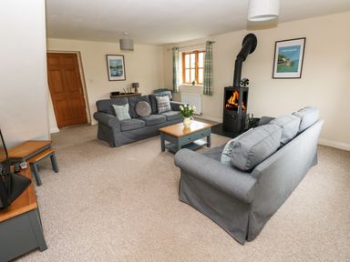 A living room with two grey sofas a wood burning stove and a wooden coffee table at Ty Rhosyn in Penycwm near Solva