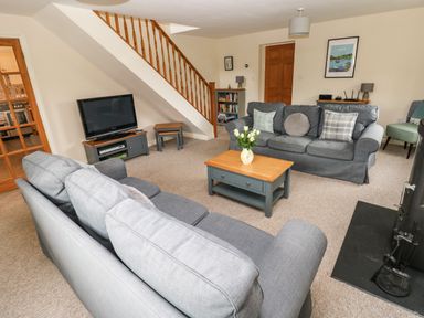 A living room with two grey sofas a wooden coffee table with flowers a television under stairs and a stove at Ty Rhosyn in Penycwm near Solva
