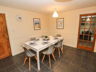 A dining room with a white table set for six and gray chairs at Ty Rhosyn in Penycwm near Solva