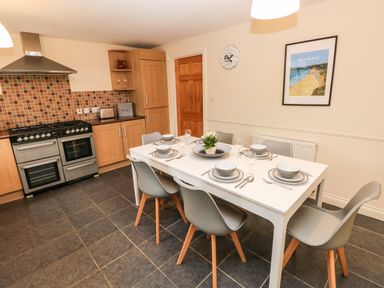 A kitchen with a dining table set for six and a stove with tiled backsplash at Ty Rhosyn in Penycwm near Solva