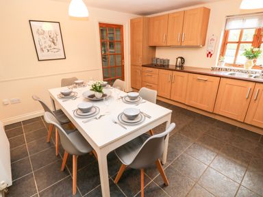 A kitchen with a white dining table set for six and wooden cabinets at Ty Rhosyn in Penycwm near Solva