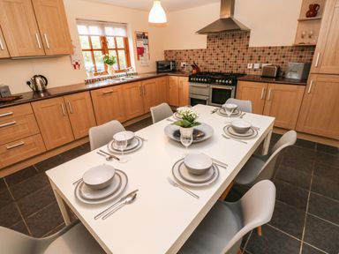 A kitchen with a white dining table set for six and wooden cabinets at Ty Rhosyn in Penycwm near Solva