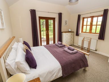 A bedroom with a double bed with purple pillows and blanket next to a window and glass doors at Ty Rhosyn in Penycwm near Solva
