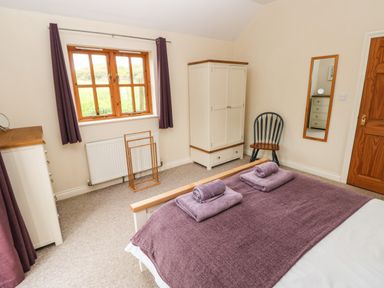 A bedroom with a bed covered in purple towels a white wardrobe a chair a dresser a window with purple curtains and a wall mirror at Ty Rhosyn in Penycwm near Solva