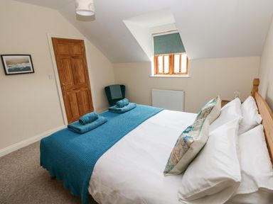 A bedroom with a double bed with blue throws and pillows a wooden door a chair a window with blind and a radiator at Ty Rhosyn in Penycwm near Solva
