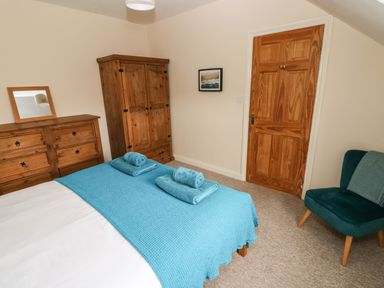 A bedroom with a bed covered with blue blankets and towels a wooden dresser with a mirror a wooden wardrobe a wooden door and a teal armchair at Ty Rhosyn in Penycwm near Solva