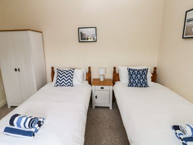 A bedroom with two single beds each with a blue patterned pillow and rolled towels a bedside table with a lamp and a white wardrobe at Ty Rhosyn in Penycwm near Solva