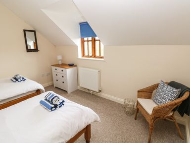 A bedroom with two single beds towels on beds a chest of drawers a wicker chair and a window at Ty Rhosyn in Penycwm near Solva