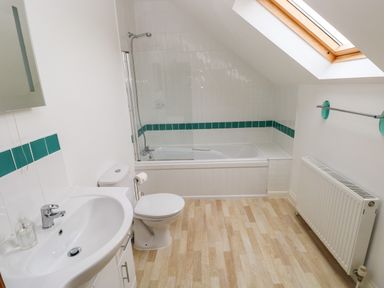 A bathroom with a sink, toilet, bathtub with shower, skylight window, radiator, and green tile accents at Ty Rhosyn in Penycwm near Solva