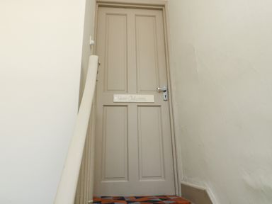 A closed beige door with a sign labeled Upper Oakwood at the top of a carpeted staircase in a hallway at Upper Oakwood in Alnwick