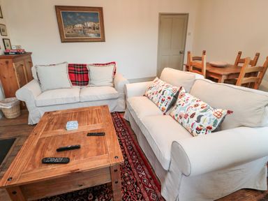 A living room with two white sofas, a wooden coffee table, a dining table with chairs, and framed pictures on the wall at Upper Oakwood in Alnwick