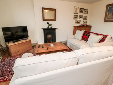 A living room with two white sofas a wooden coffee table a television on a wooden chest and a black fireplace at Upper Oakwood in Alnwick