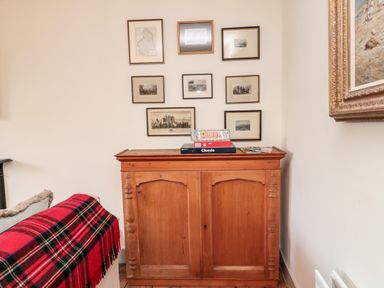 A wooden cabinet with framed pictures above and board games on top next to a sofa with a red plaid blanket at Upper Oakwood in Alnwick