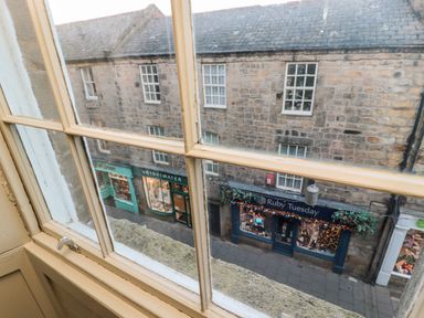 A view through a window showing stone buildings with shop fronts named Brightwater and Ruby Tuesday at Upper Oakwood in Alnwick