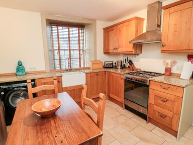 A kitchen with wooden cabinets a dining table with chairs a sink and cooking stove at Upper Oakwood in Alnwick