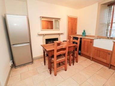 A kitchen with a wooden dining table and two chairs a refrigerator wooden cabinets and a sink at Upper Oakwood in Alnwick