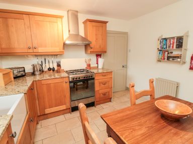 A kitchen with wooden cabinets a stove a table with chairs and a bookshelf on the wall at Upper Oakwood in Alnwick