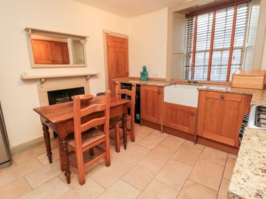 A kitchen with wooden cabinets a farmhouse sink a wooden table with chairs a window with blinds a small statue on the counter and a mirror above a fireplace at Upper Oakwood in Alnwick