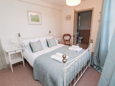 A bedroom with a double bed blue quilt wooden chair bedside tables and an open door to a bathroom at Upper Oakwood in Alnwick