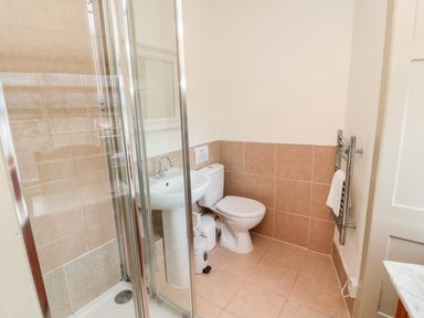 A bathroom with a shower enclosure a pedestal sink a toilet a towel rail and beige tiled walls at Upper Oakwood in Alnwick