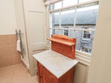 A bathroom corner with a wooden cabinet topped with marble near a window and a towel rack with a towel on a tiled wall at Upper Oakwood in Alnwick