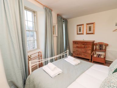 A bedroom with a bed, wooden chest of drawers, chair, and curtains at Upper Oakwood in Alnwick