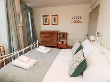 A bedroom with a bed with folded towels wooden dresser and chair and curtains at Upper Oakwood in Alnwick