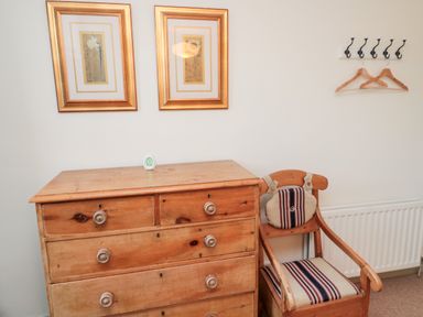 A wooden chest of drawers next to a wooden chair with striped cushions under two framed pictures on a wall with coat hooks at Upper Oakwood in Alnwick