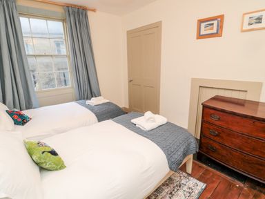 A bedroom with two single beds with gray blankets and pillows next to a window with blue curtains and a wooden dresser at Upper Oakwood in Alnwick
