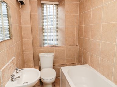 A bathroom with a white sink, toilet, bathtub, tiled walls, and a window with blinds at Upper Oakwood in Alnwick