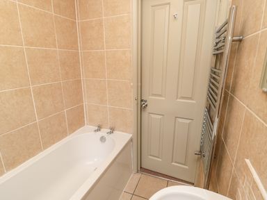 A bathroom with a white bathtub chrome taps beige tiled walls a white door and a chrome heated towel rail at Upper Oakwood in Alnwick