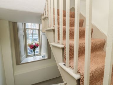 A staircase with beige carpet and a window with flowers in a vase on the sill at Upper Oakwood in Alnwick