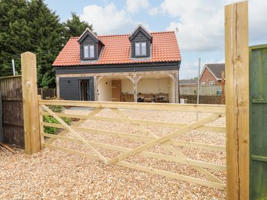 A gravel driveway with a wooden gate leading to a black house with a red roof and two dormer windows at Strawberry Fields Annex in Emneth