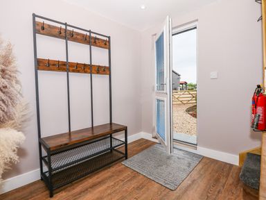An entryway with a wooden bench coat rack a grey floor mat an open door leading outside and a fire extinguisher mounted on the wall at Strawberry Fields Annex in Emneth