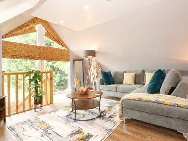 A living room with a gray sofa blue and yellow pillows a round wooden coffee table and a large window with orange patterned blinds at Strawberry Fields Annex in Emneth