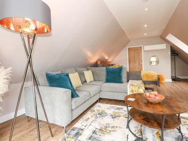 A living room with a grey sectional sofa with cushions a wooden coffee table with a bowl of apples a floor lamp and wooden flooring at Strawberry Fields Annex in Emneth