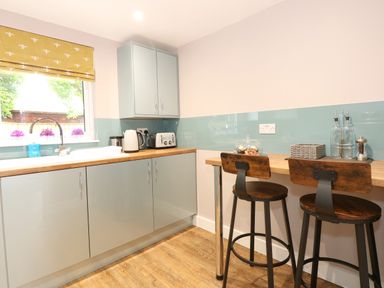 A kitchen with light blue cabinets wooden countertop and two wooden bar stools at Strawberry Fields Annex in Emneth