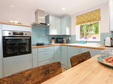 A kitchen with blue cabinets wooden countertops a built in oven microwave sink and a wooden table with chairs at Strawberry Fields Annex in Emneth