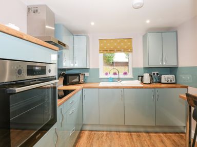 A kitchen with light blue cabinets wooden countertops an oven microwave toaster kettle and a window with a yellow blind at Strawberry Fields Annex in Emneth