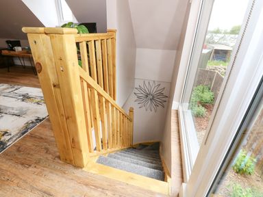 A wooden staircase with grey carpet next to a large window and a wall decoration at Strawberry Fields Annex in Emneth