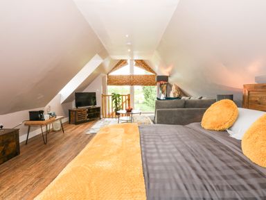 A loft bedroom with a bed and orange pillows and a gray sofa with a tv on a wooden stand at Strawberry Fields Annex in Emneth
