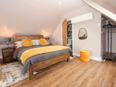 A bedroom with a wooden bed with yellow pillows and blanket bedside tables lamps a mirror an air conditioner and a clothing rack at Strawberry Fields Annex in Emneth