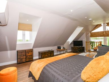 A bedroom with a bed gray bedding and orange pillows and throw a TV on a stand and a small table near a window at Strawberry Fields Annex in Emneth