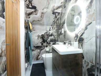 A bathroom with a wooden door a floating vanity with sink a round illuminated mirror a toilet and towels at Strawberry Fields Annex in Emneth