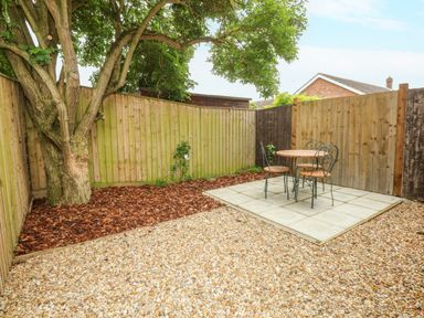 A backyard with a tree surrounded by mulch a small patio with a round table and two chairs and gravel ground at Strawberry Fields Annex in Emneth