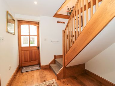 A hallway with wooden stairs a wooden door and a mirror on the wall at Oak Barn in Kentisbeare