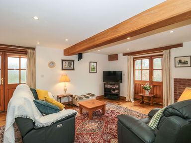 A living room with leather sofas, a wooden coffee table, a television, and wooden doors at Oak Barn in Kentisbeare