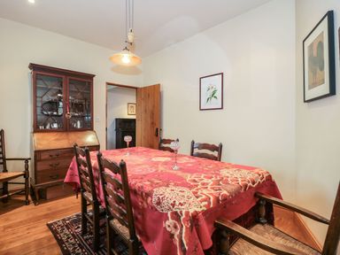 A dining room with a red patterned tablecloth on a table surrounded by wooden chairs wooden cabinet and framed pictures on the walls at Oak Barn in Kentisbeare