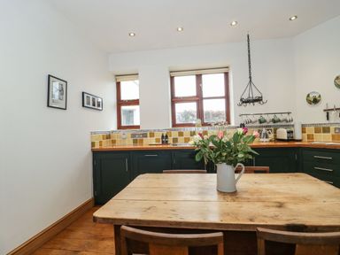 A kitchen with wooden dining table and flowers in a jug on it at Oak Barn in Kentisbeare