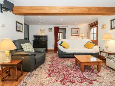 A living room with sofas coffee table lamps wooden beams and a patterned rug at Oak Barn in Kentisbeare